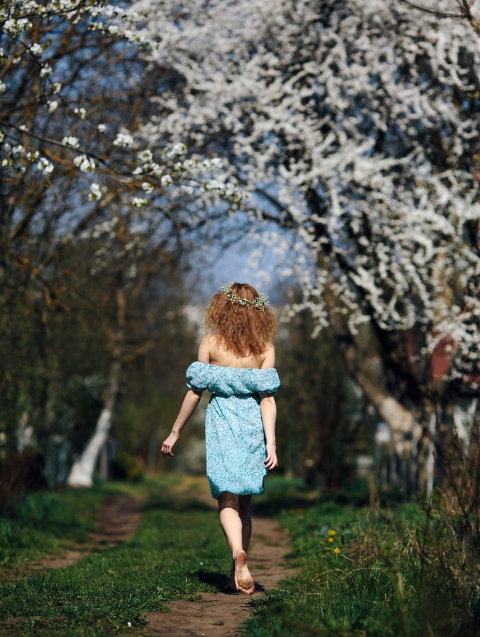 beautiful girl walks in the lush garden dressed in a wreath